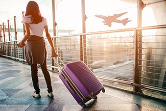 A woman rolls her suitcase through an airport as a plane takes off outside the window